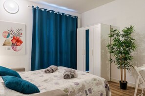 Een slaapkamer met een bed, een blauw gordijn, een kledingkast, een kamerplant en een kunstwerk aan de muur.