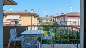 Un balcon avec deux chaises blanches et une table, donnant sur un quartier résidentiel avec des maisons et de la verdure.