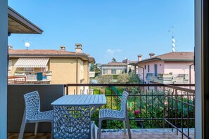 Un balcon avec deux chaises blanches et une table, donnant sur un quartier résidentiel avec des maisons et de la verdure.