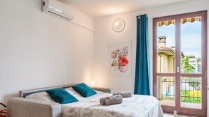 Une chambre avec un lit, un extincteur, un climatiseur fixé au mur, une fenêtre avec des rideaux et une vue sur l’extérieur.