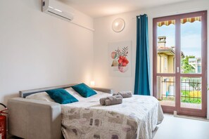 Une chambre avec un lit, un extincteur, un climatiseur fixé au mur, une fenêtre avec des rideaux et une vue sur l’extérieur.