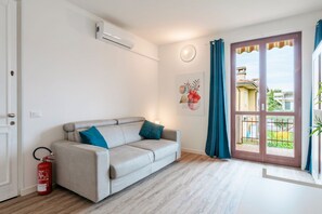 Un salon moderne avec un canapé beige, un extincteur, une fenêtre avec des rideaux et un climatiseur fixé au mur.