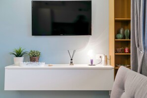 A modern living room with a mounted TV, a white console table with decorative items, a potted plant, and a cacti shelf.
