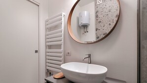 Un baño moderno con un lavabo blanco tipo recipiente, un espejo redondo con marco de madera y un perchero para toallas.