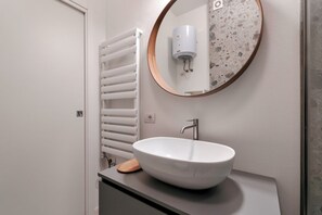 A modern bathroom with a white vessel sink, a round mirror with a wooden frame, and a towel rack.