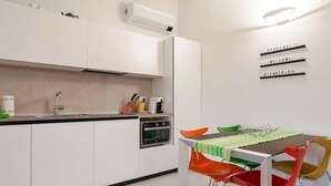 Una cocina moderna con armarios blancos, horno integrado y comedor con sillas coloridas y una mesa.