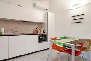 A modern kitchen with white cabinets, a built-in oven, and a dining area with colorful chairs and a table.