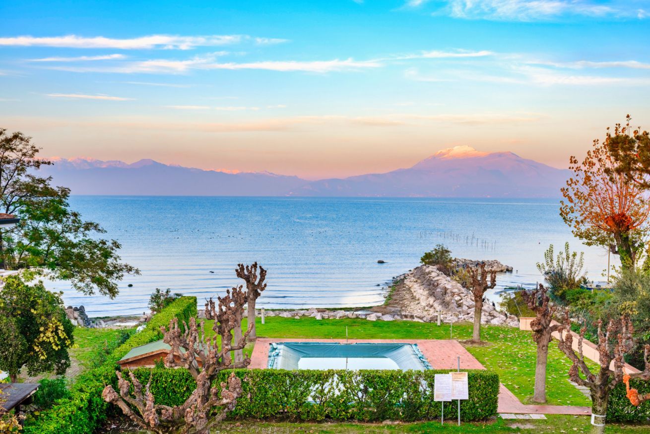 A coastal view with a swimming pool, green lawns, and a mountainous backdrop.