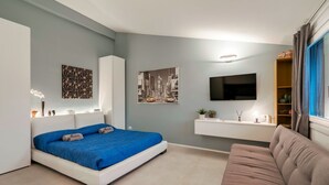 Un dormitorio moderno con una cama, un sofá, un televisor y un pequeño estante con objetos decorativos.