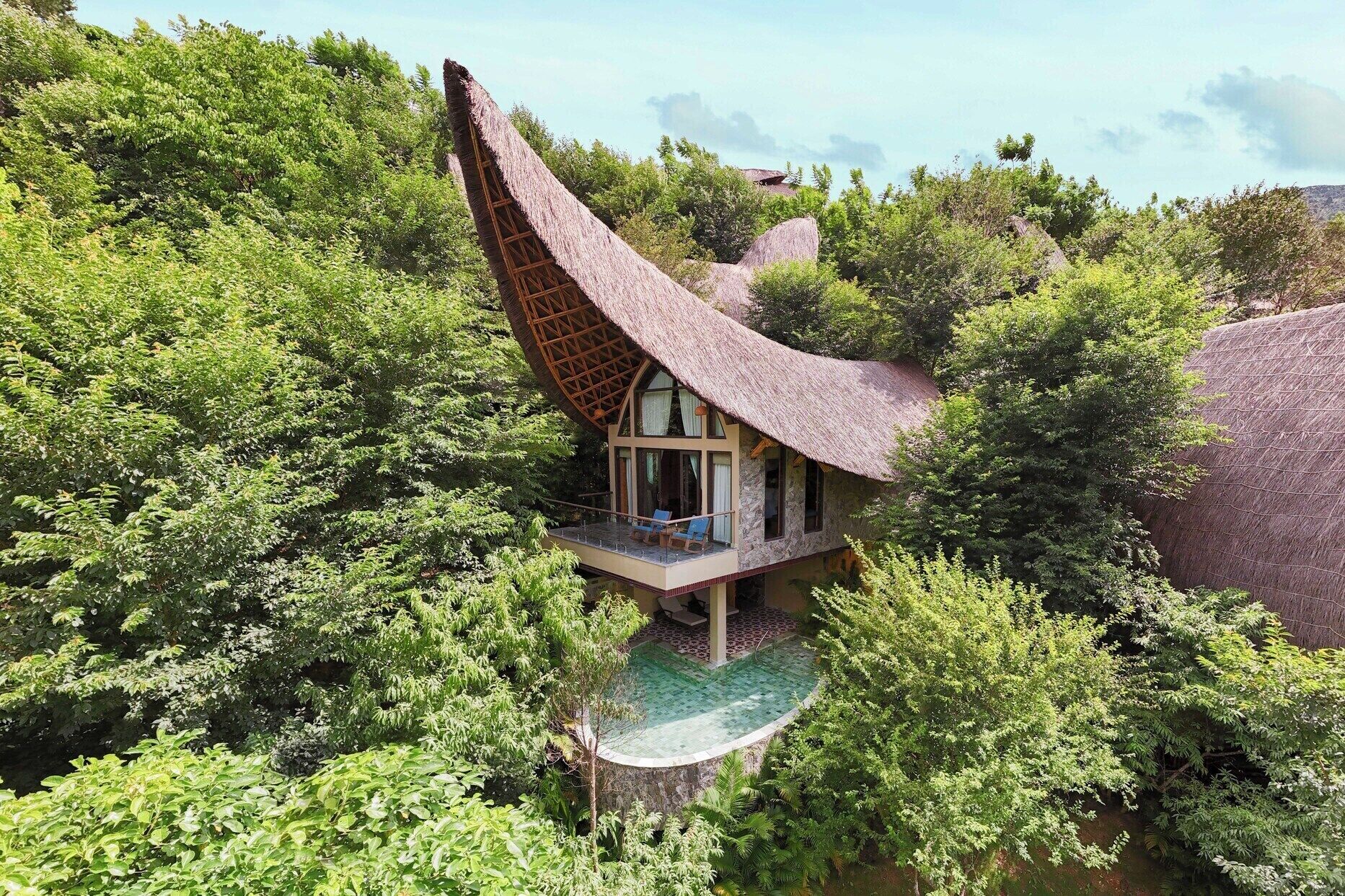 A house with a unique curved roof, surrounded by lush greenery.