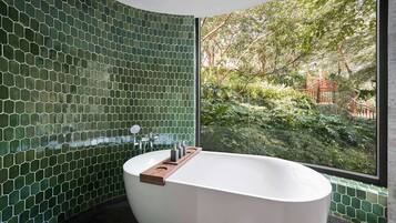 Um banheiro moderno com banheira livre, azulejos de mosaico verde e vista para um jardim exuberante através de uma grande janela.