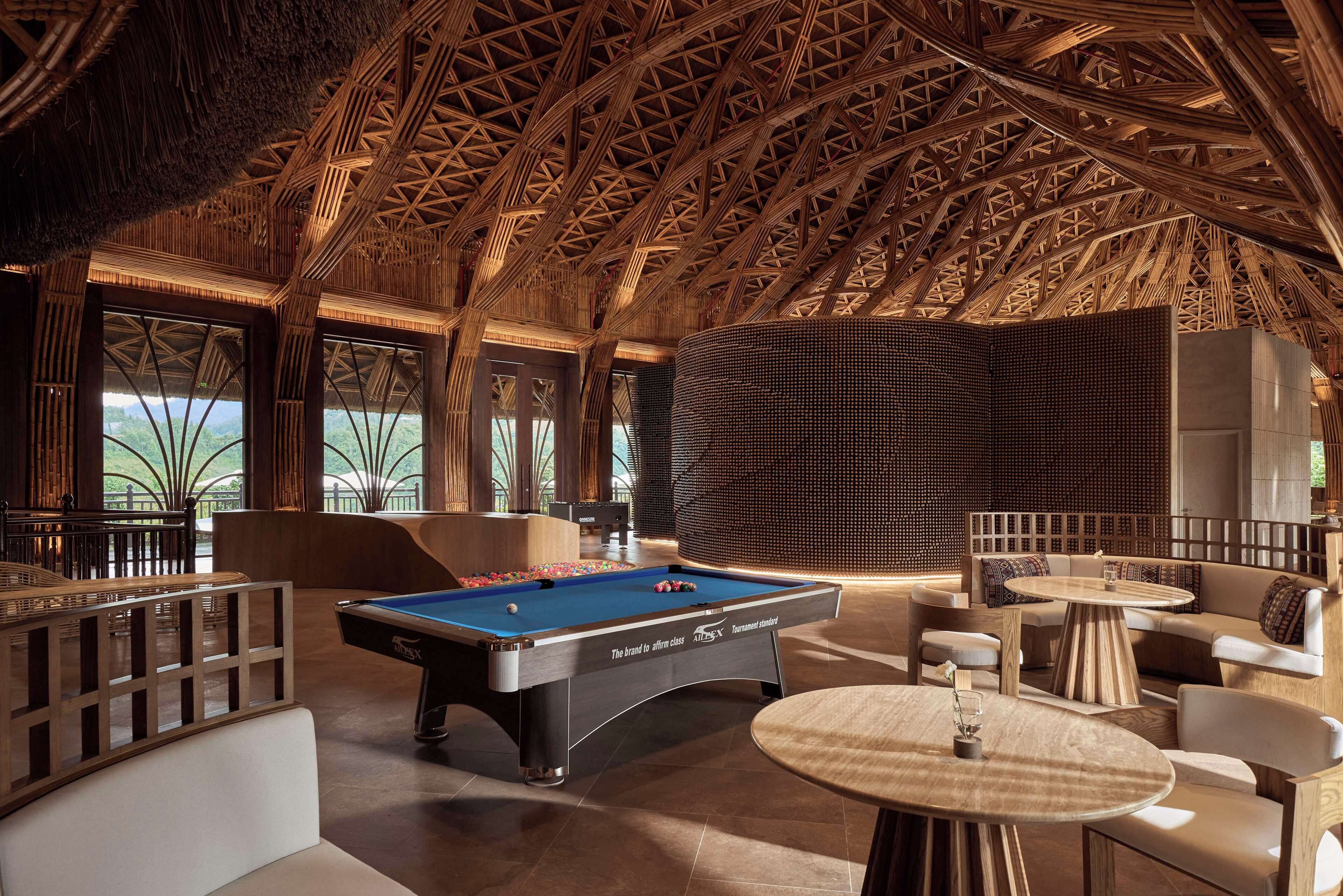 Ein Billardtisch in einem Raum mit hoher Decke und Holzbalken. Um den Billardtisch stehen Sofas und Tische.