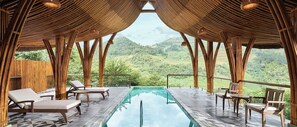 A pool area with lounge chairs and tables, surrounded by bamboo structures, overlooking a lush green landscape. - Garrya Mu Cang Chai (Mu Cang Chai)
