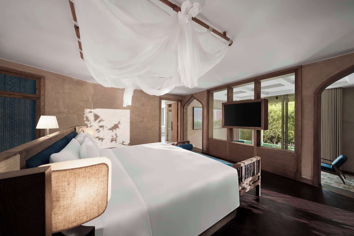 A modern hotel room with a large bed, a flat-screen TV, and large windows offering a view of the outdoors.
