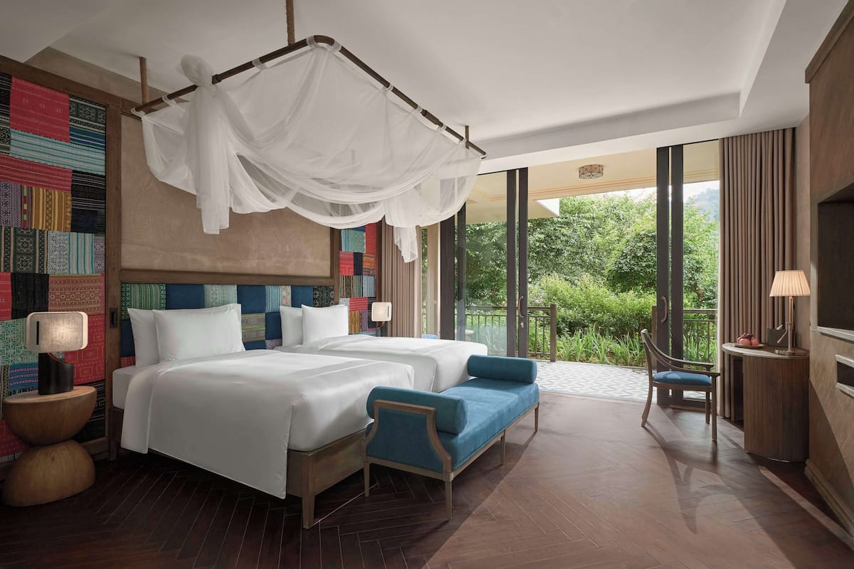 Una habitación de hotel moderna con una cama grande, un sofá cama, una cama con dosel, un televisor y vistas a zonas verdes.