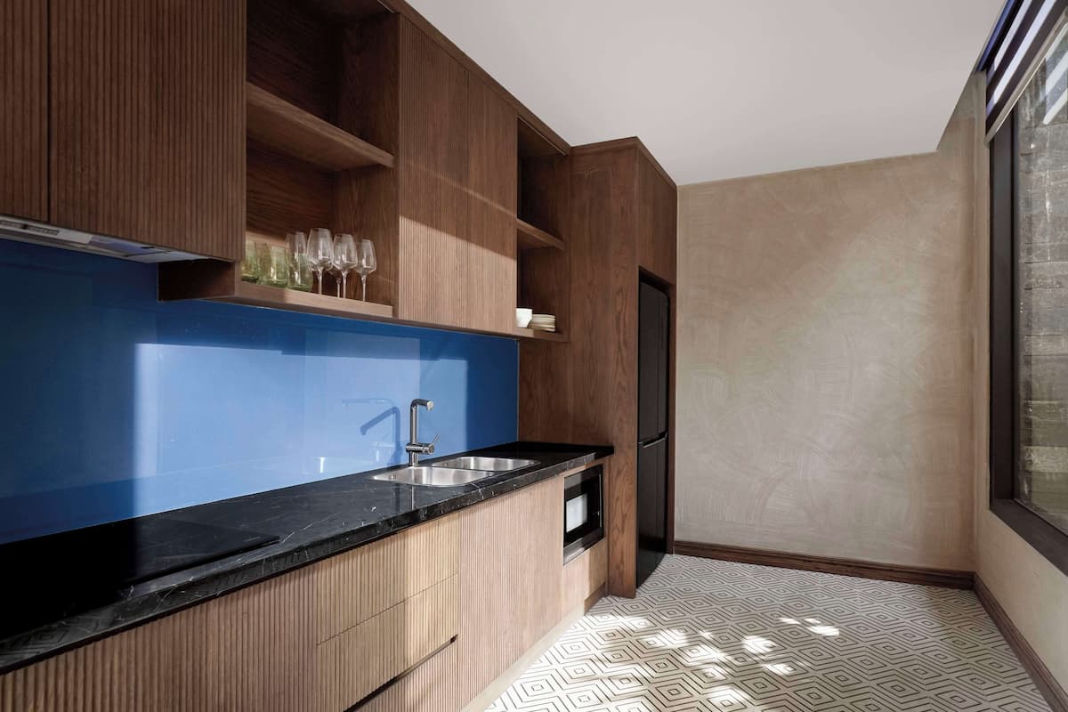A modern kitchen with wooden cabinetry, a black countertop, a built-in oven, and a stainless steel sink.
