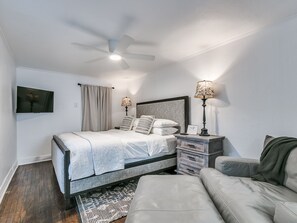 Una camera da letto con un letto, comodini, un ventilatore a soffitto, una televisione e un divano.