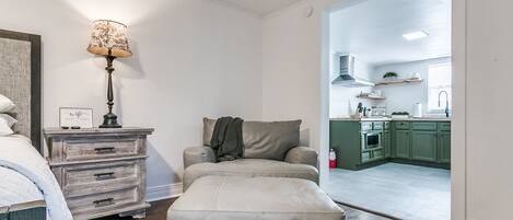 Una sala de estar acogedora con un sofá, una lámpara y una mesita auxiliar. Se ve una cocina a través de un vano abierto.