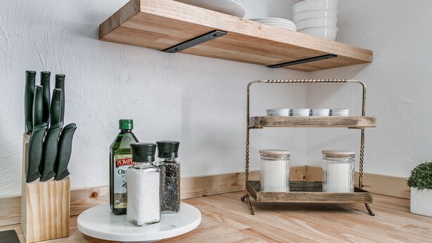 Une cuisine avec des étagères en bois, un bloc à couteaux, des pots à épices et une étagère métallique contenant des bocaux.