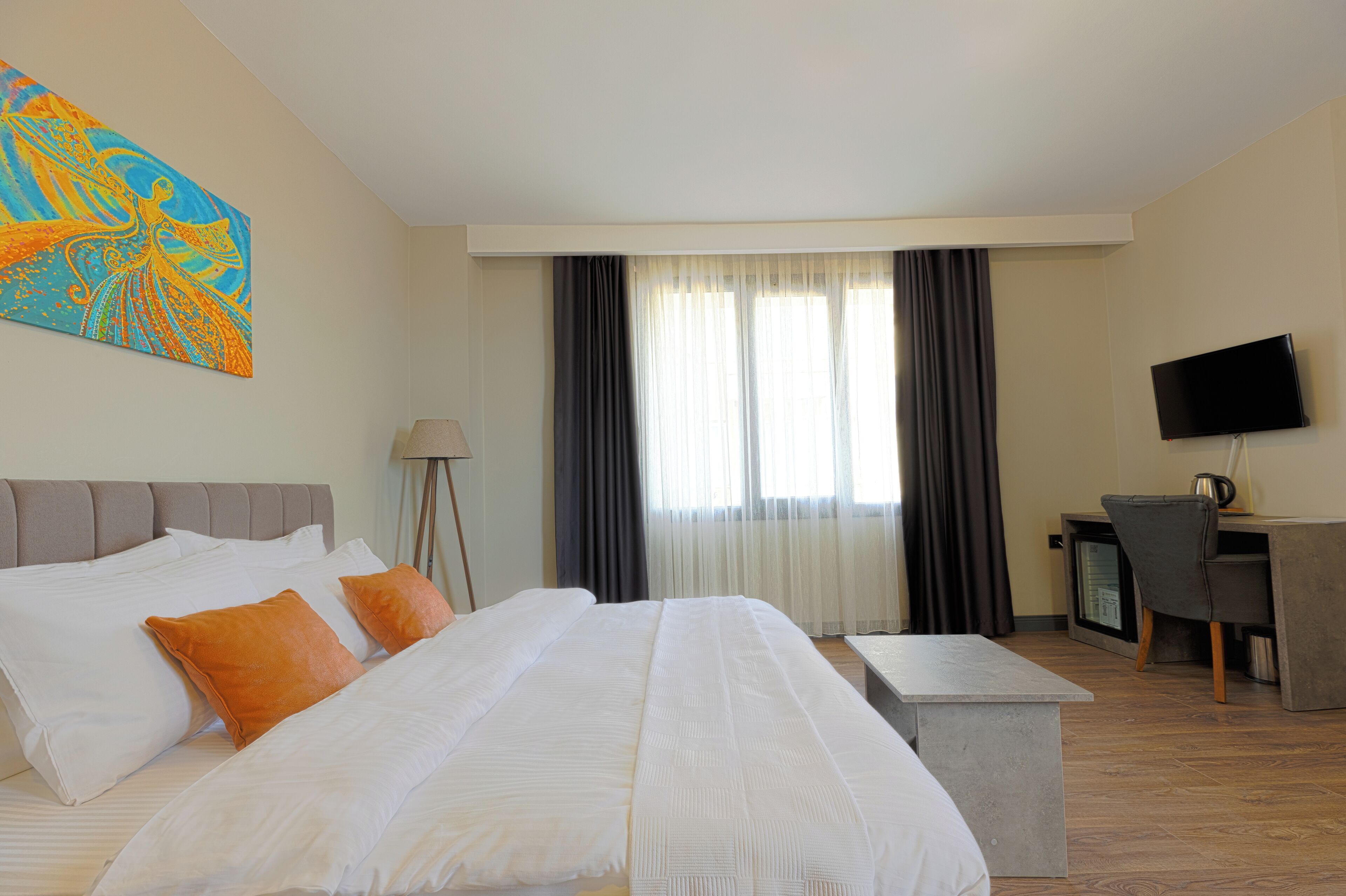 A hotel room with a large bed, a desk, a television, and a painting on the wall.