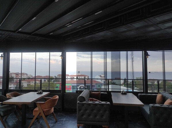 A restaurant with large windows offering a view of the sea and buildings.