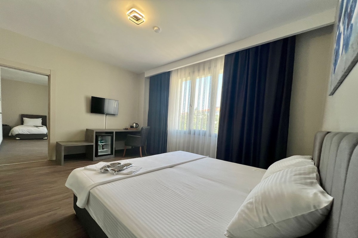 A hotel room with a bed, a desk, a chair, a television, and a window with curtains.
