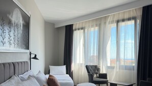 A hotel room with a large bed, a desk, a chair, and a view of the outdoors. - Grand Royal Hotel (Silivri)