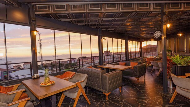 A modern interior with large windows, seating areas, and a view of the cityscape. - Grand Royal Hotel (Silivri)