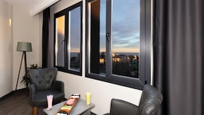 A modern living room with two leather armchairs, a small table with a tray of snacks, and a view of the city through large windows. - Grand Royal Hotel (Silivri)