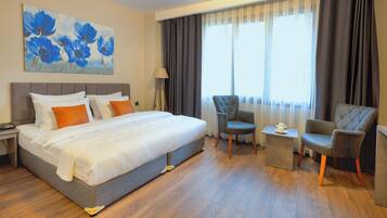 Habitación de hotel con una cama grande, dos sillones, una mesita auxiliar y un cuadro de flores azules en la pared.