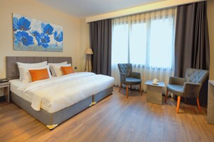 Habitación de hotel con una cama grande, dos sillones, una mesita auxiliar y un cuadro de flores azules en la pared.