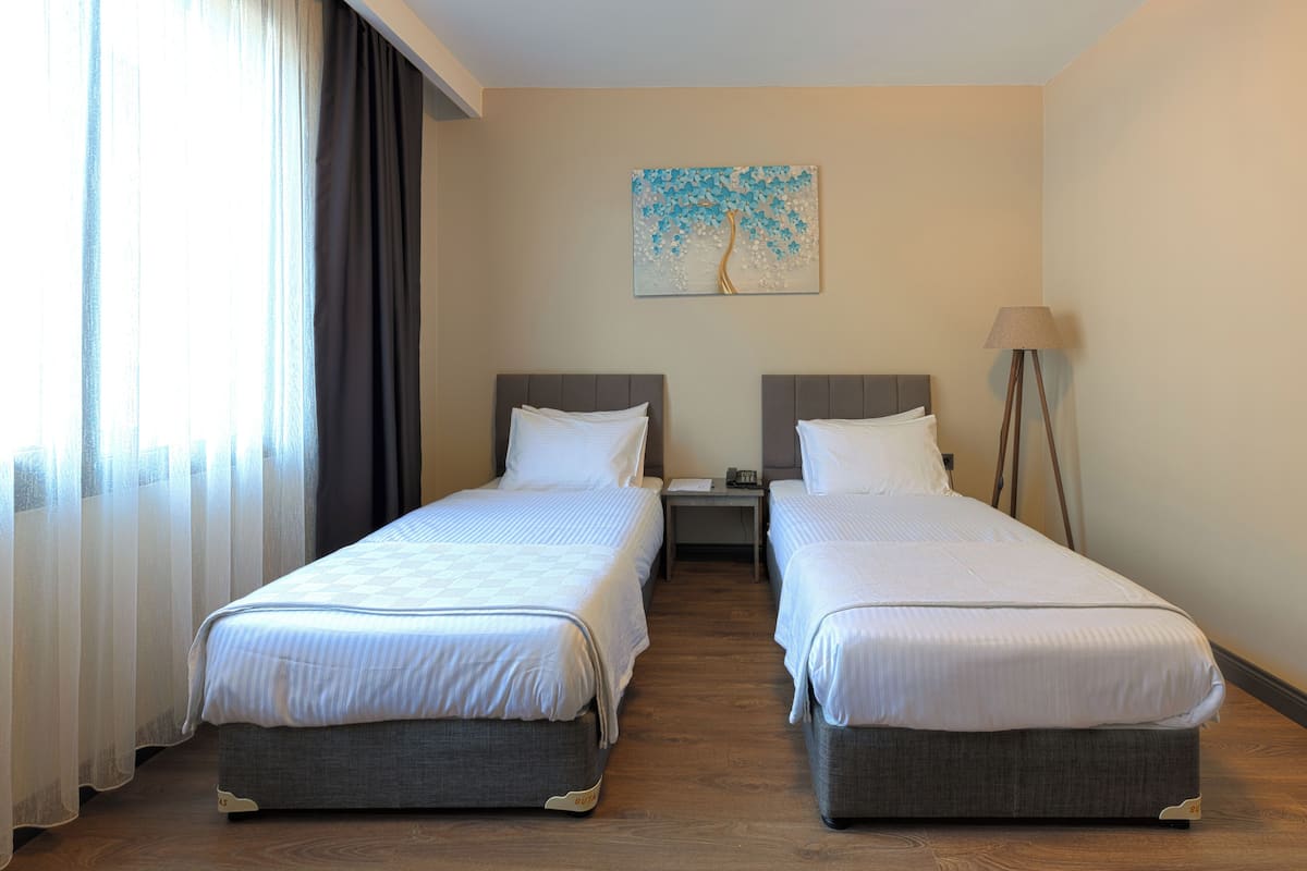 A hotel room with two beds, a nightstand, a lamp, and a painting on the wall.