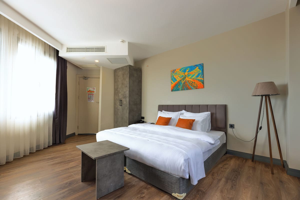 A modern hotel room with a large bed, a bedside table, a lamp, and a painting on the wall.