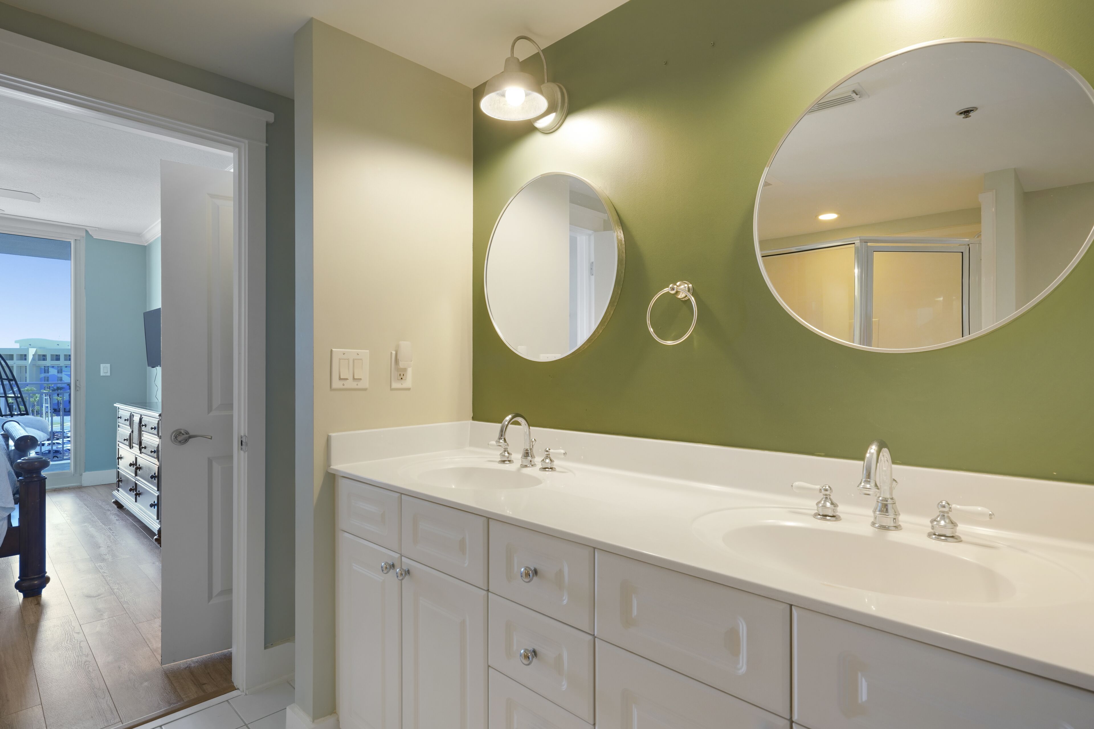 Une salle de bain avec deux lavabos, un grand miroir et une porte donnant sur un couloir.