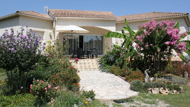Une maison avec un chemin de pierre menant à un patio couvert, où se trouvent une table et des chaises.