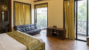 Ein Schlafzimmer mit einem Bett, einer Couch, einem kleinen Schrank und einem Balkon mit Vorhängen.