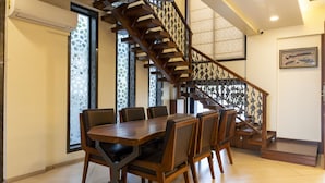 Ein Essbereich mit Holztisch und -stühlen, eine Treppe mit einem gemusterten Geländer und ein Fenster mit geometrischem Design.