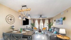 Un salon moderne avec un coin repas, comprenant un téléviseur à écran plat, un ventilateur de plafond et un grand tableau accroché au mur.