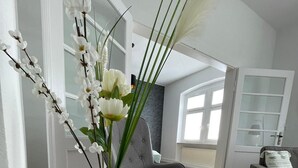 A modern living room with a round coffee table, a grey armchair, and a sofa. There is a vase with white flowers on the table. - Modernes, Großes City Apartment 95 qm in Meuselwitz (Meuselwitz)
