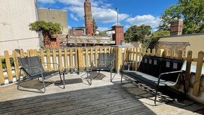 A wooden deck with outdoor seating and a view of a brick chimney and trees. - Modernes, Großes City Apartment 95 qm in Meuselwitz (Meuselwitz)