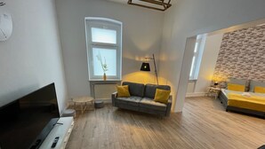 A modern living room with a flat-screen TV, a grey sofa with yellow cushions, a small round table, and a lamp. - Modernes, Großes City Apartment 95 qm in Meuselwitz (Meuselwitz)