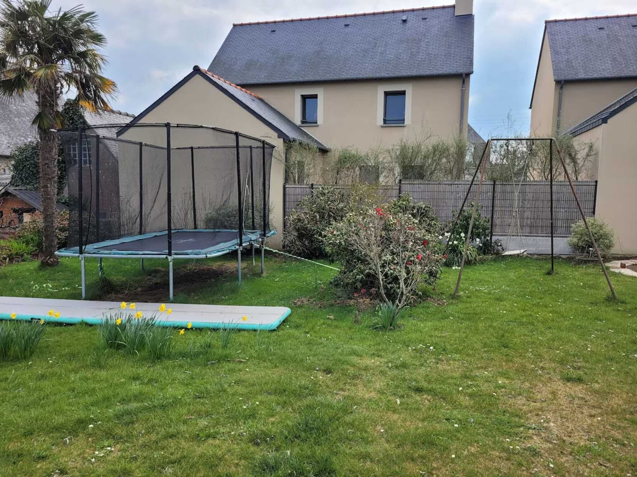 A backyard with a trampoline, a small garden, and a house with a grey roof.