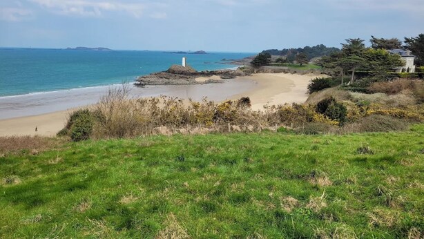 A coastal landscape with a sandy beach, grassy areas, and a lighthouse in the distance. - Appartement à 80 Mètres de la Mer, Chez L'habitant, en Rez-de-jardin (Saint-Lunaire)