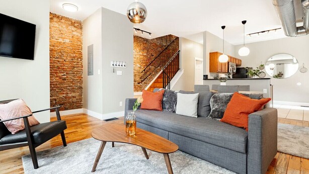 Un salon moderne avec un canapé gris, une table basse en bois et un mur décoratif en briques.
