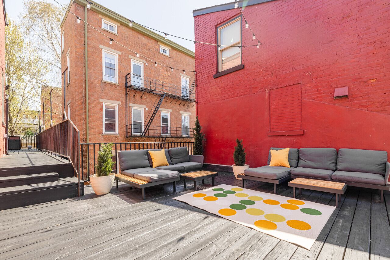 A rooftop deck with outdoor seating, a red building, and a brick building in the background.