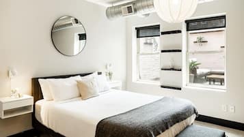 Une chambre moderne avec un grand lit, une table de chevet, un miroir et une fenêtre donnant sur l’extérieur.