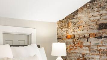 Een hotelkamer met een bed, witte kussens, een witte lamp en een stenen muur.