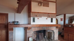 Ein traditioneller Kamin mit Ziegelverkleidung, einem Holzbalken darüber und einem kleinen Fenster mit dekorativem Gitter.