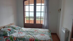 Ein Schlafzimmer mit einem mit Blumenmuster bezogenen Bett, einem Fenster mit Vorhängen und einer Heizung.