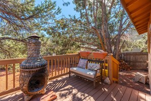 Une terrasse en bois avec un foyer en pierre et un banc agrémenté de coussins.